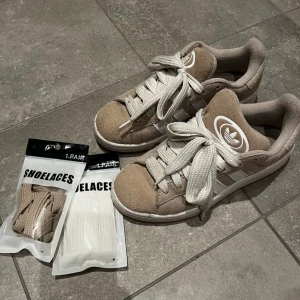 Beige sneakers från Adidas - Säljer ett par adidas campus 00 i storlek 38! Använda en halv sommar så i väldigt fint skick! Ingår ett nytt par vita breda snören, samt tunna beigea💕
