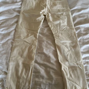 Beige jeansbyxor - Snygga beige jeansbyxor med en klassisk design. De har en rak passform och är perfekta för en avslappnad stil. Byxorna har fickor både fram och bak, vilket ger en praktisk touch.