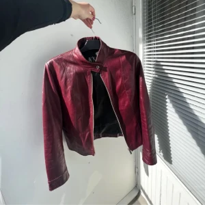 Vinröd skinnjacka - Snygg vinröd skinnjacka från KS med dragkedja och ståkrage. Jackan har långa ärmar och en stilren design som passar perfekt för höst och vår. Perfekt för att ge din outfit en cool touch!