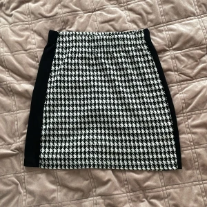 Svartvit kjol från Lindex - Snygg svartvit kjol från Lindex med klassiskt hundtandsmönster. Kjolen har en tight passform och är perfekt för en stilren look. Tillverkad i ett bekvämt material som passar både till vardag och speciella tillfällen.