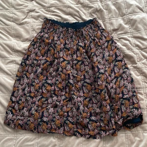 Mönstrad kjol från InWear - Snygg kjol från InWear med ett färgglatt blommönster i rosa, orange och vitt på en mörkblå bas. Kjolen har en elastisk midja för bekväm passform och är perfekt för både vardag och speciella tillfällen. Ett måste i garderoben för den som älskar färg och mönster!