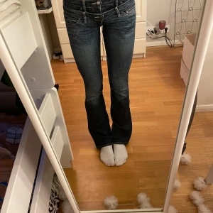 Mörkblå bootcut jeans - Snygga mörkblå bootcut jeans med låg midja och klassisk femficksdesign. Jeansen har en lätt tvättad look och passar perfekt för en avslappnad stil. De är tillverkade i ett slitstarkt denimtyg och har en bekväm passform.