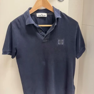 Mörkblå pikétröja från Stone Island - Snygg mörkblå pikétröja från Stone Island i slim fit. Tröjan har en klassisk krage och knappar framtill. 