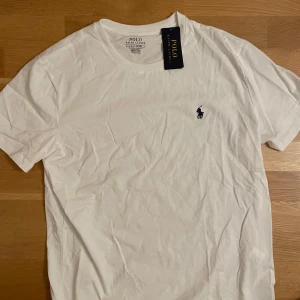 Vit t-shirt från Polo Ralph Lauren - Säljer en klassisk vit t-shirt från Polo Ralph Lauren med det ikoniska broderade logotypen på bröstet. T-shirten är kortärmad och tillverkad i mjuk bomull för en bekväm passform. Perfekt för en stilren och avslappnad look.