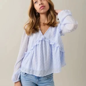 Ljusblå blus med volangdetaljer - Säljer en söt ljusblå blus med volangdetaljer och prickigt mönster. Blusen har långa ärmar och en v-ringad design. 