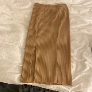 Beige ribbad kjol - Snygg beige ribbad kjol med en stilren slits framtill. Perfekt för en chic och avslappnad look. Kjolen har en smickrande passform och är enkel att matcha med olika toppar.
