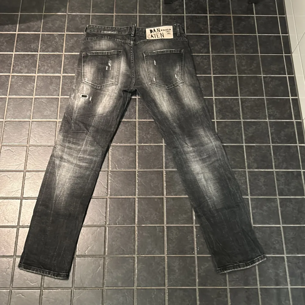 Snygga svarta jeans från DSQUARED2 med slitna detaljer och en cool tvättad look. De har en dragkedja och knappar framtill samt klassiska fem fickor. Perfekta för en trendig stil. Storlek 46 passar som 31/32.. Farkut & Housut.