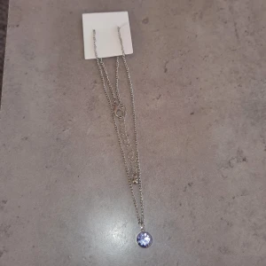 Silverfärgat halsband - Elegant silverfärgat halsband med en vacker lila sten som hänge. Kedjan är tunn och stilren, vilket gör det till ett perfekt smycke för att lyfta vilken outfit som helst.