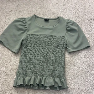 Grön topp från Gina Tricot - Grön topp från Gina Tricot i storlek XS. Toppen har korta ärmar som jsg sydde om från långärmad därför ser man stygnen. Toppen är smockad.