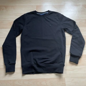 Svart tröja från GANT - Säljer en stilren svart tröja från GANT. Tröjan har långa ärmar och en rund halsringning med ribbade muddar. Perfekt för en avslappnad och snygg look.