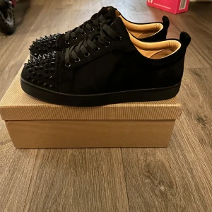Louboutin skor - Snygga svarta sneakers med nitar på tån och snörning. Perfekta för att ge en edgy touch till din outfit. Skorna har en stilren design med en låg profil och är tillverkade i ett material som ser ut som mocka. 4 taggar som åkt av men det medföljer taggar som man kan sätta dit 