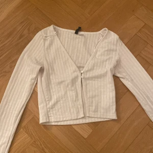 Vit ribbad kofta från H&M Divided - Säljer en söt vit ribbad kofta från H&M Divided. Den har en v-ringad design med knappar framtill och långa ärmar. Perfekt för lager-på-lager-stil eller som ett lättare plagg för svalare dagar.