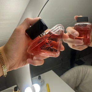 Prada Paradoxe Intense Eau de Parfum - Säljer en elegant Prada Paradoxe Intense Eau de Parfum. Flaskan har en unik triangulär form med en svart kork och rödaktig vätska. Förpackningen är stilren i rosa med svart text. Perfekt för den som älskar lyxiga dofter. Oanvänd, köptes för 1400 ca