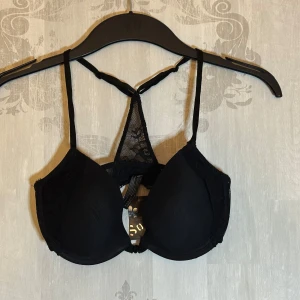 Ny Svart och rosa bh från So.U - Snygg svart bh med rosa insida från So.U. Den har spetsdetaljer och justerbara axelband för perfekt passform. Perfekt för att ge en färgklick till din underklädeskollektion.