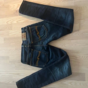 Mörkblå jeans med orange sömmar - Snygga mörkblå nudie jeans med kontrasterande orange sömmar och klassisk femficksdesign. De har en normal passform och är perfekta för en avslappnad stil. Jeansen är väldigt snygga och passar till allt. Dom är w26 men passar mig som har 29 i flesta jeans och dom är 32 i längd. Säljer dom då jag är för kort för dom så dom sitter inte så bra på mig.pris kan gå ner vid snabb affär