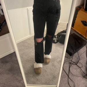 Svarta jeans med slitningar från Perfect Jeans - Snygga svarta jeans från Perfect Jeans med slitningar på knäna för en trendig look. De har en klassisk femficksdesign och knappar i midjan. Perfekta för en avslappnad stil.