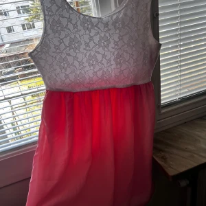 Vit och rosa klänning från Rut & Circle - Charmig klänning från Rut & Circle med vit spetsöverdel och rosa kjol. Den är ärmlös och har en söt, feminin stil. Perfekt för somriga dagar eller speciella tillfällen.