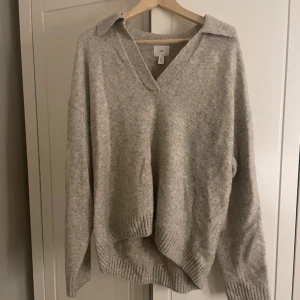 Beige  stickad tröja med krage - Säljer en mysig beige stickad tröja med v-ringning och krage. Tröjan har långa ärmar och ribbstickade muddar vid ärmslut och nederkant. Perfekt för kyliga dagar! Från hm 
