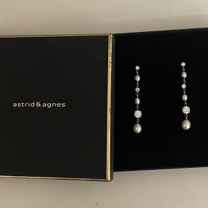 Långa örhängen från Astrid & Agnes - Säljer dessa oanvända Långa PATRICIA örhängen från Astrid & Agnes. Dessa långa örhängen består av stål på stift med vita äkta pärlor och kristaller. Passar just för dig som gillar långa örhängen med mycket detaljer av kristaller och pärlor. Längden på dessa örhängen är 6,7 cm. Ordinal pris: 799kr