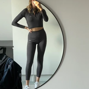 Träningsset ICIW - Mörkgrått/lila träningsset från ICANIWILL, en croppad långärmad topp och matchande högmidjade tights. De är fullängd, bara jag som har extremt kpnga ben.. Supermjukt och skönt material! Använt ett fåtal gånger, men tycker benen är för korta som sagt (är 177)