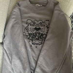 Grå sweatshirt från Kenzo - Säljer en grå sweatshirt från Kenzo med ett coolt tigerbroderi på framsidan. Tröjan har långa ärmar och en rund halsringning. Använd 1-2 gånger, tvättad, inga fläckar!💕