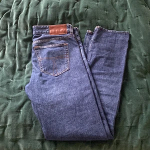 Tiger of Sweden - Blåa jeans - Snygga blå jeans från Tiger of Sweden med klassisk femficksdesign och en läderdetalj vid midjan. Perfekta för en stilren look. Passar till det mesta och är ett riktigt bra kap. Skick: 8/10