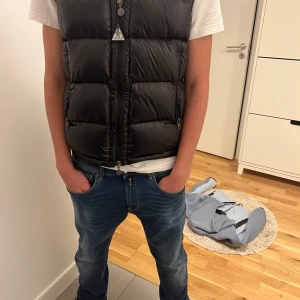 Svart dunväst med huva - Säljer en snygg svart dunväst i mycket bra skick. Västen har en dragkedja framtill och en praktisk huva. Perfekt för höst och vår när du vill hålla dig varm men ändå se stilren ut. Passar bra till både jeans och chinos.