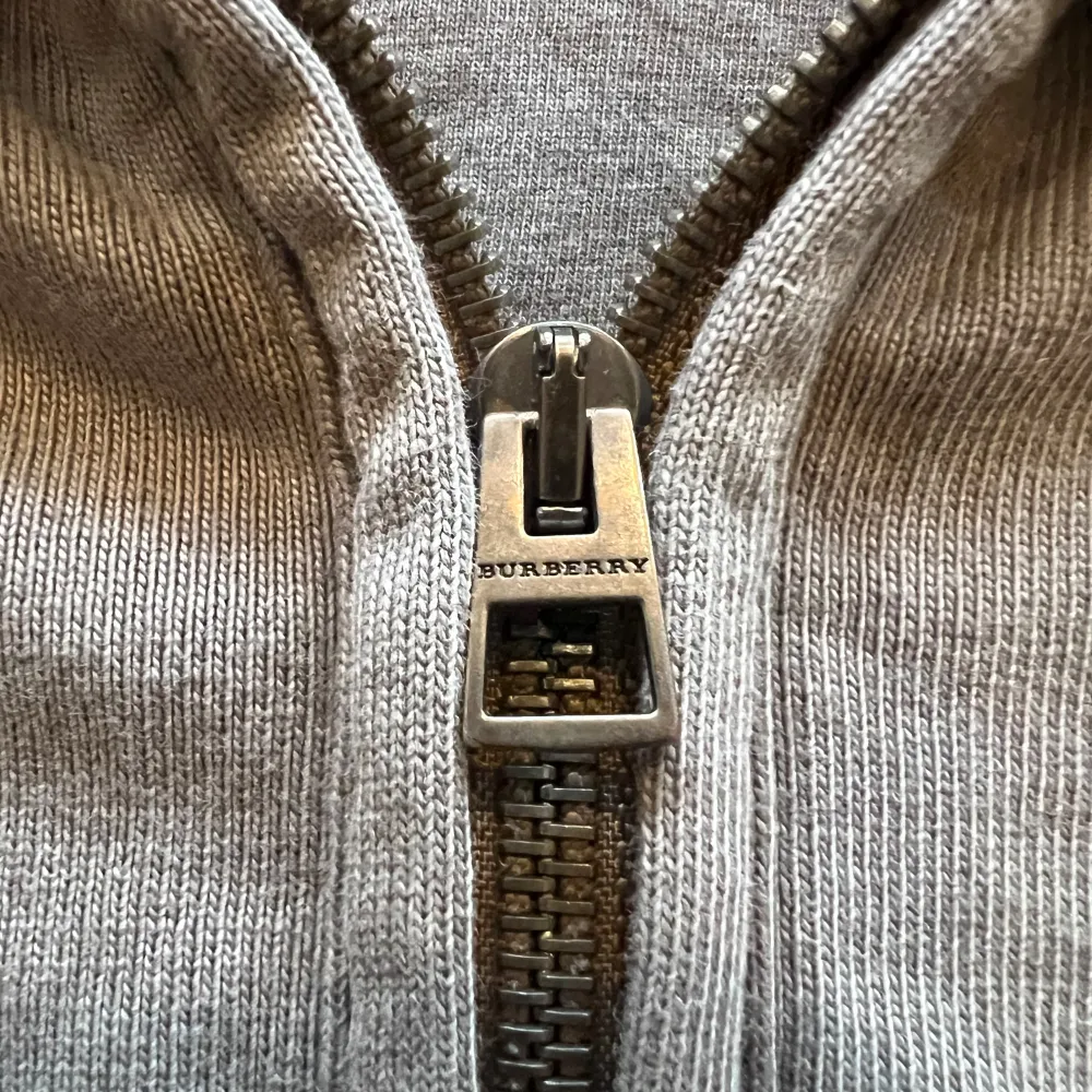 Säljer en snygg grå hoodie från Burberry i 100% bomull. Den har en dragkedja framtill och coola rutiga detaljer på armbågarna och insidan av huvan. Perfekt för höst och vår när du vill vara både bekväm och stilren. Passar lika bra till jeans som till mjukisbyxor. Pris kan diskuteras!. Tröjor & Koftor.