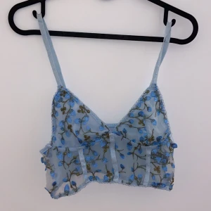 Blå blommig spetslinnetopp - Säljer en superfin blå linnetopp med blommigt broderi. Toppen har smala axelband och är perfekt för sommardagar. Den är gjord i ett lätt och luftigt material med spetsdetaljer som ger en romantisk känsla. Passar perfekt till både jeans och kjol!