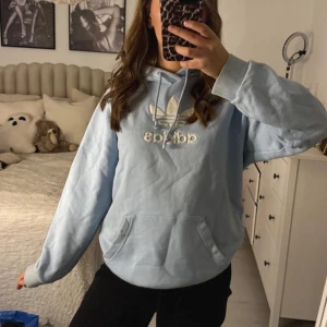 Ljusblå hoodie från Adidas - Mysig ljusblå hoodie från Adidas med den klassiska loggan i vitt framtill. Finns en sminkfläck inuti hoodie som jag tror går bort med vanish men inget som syns när man har på den 