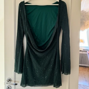 Grön kort glitterklänning med öppenrygg - Superfin grön glitterklänning perfekt för nyår eller jul! Klänningen är kort och har en murgrön färg & en superfin öppen rygg med snörning (se 2:a bild) 🤍 Använd bara en gång så är i nytt skick, vet tyvärr inte märket på klänningen🤍