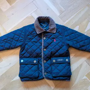 Säljer en superfin mörkblå quiltad jacka från Ralph Lauren i storlek 12M. Jackan har en snygg krage i manchester och knappar med logga. Perfekt för höst och vår! Tillverkad i 100% polyester, vilket gör den både varm och lätt att bära. 🧥✨