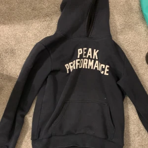 Svart hoodie från Peak Performance - Säljer en svart hoodie från Peak Performance i bra skick och storlek 160. Den har en klassisk design med vit text på bröstet och en bekväm passform. Perfekt för höst och vinter, och funkar lika bra till vardags som till träning. Fläckarna på magen går säkert bort i tvätten men det är inget som garanteras❤️ 