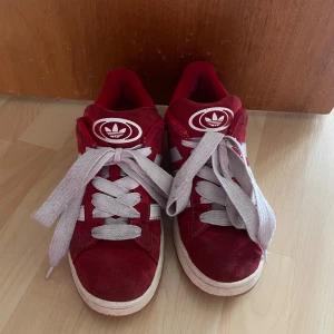 Röda Adidas Campus sneakers - Säljer ett par snygga röda Adidas Campus sneakers i mocka. Använda men i bra skick. Dem är sprayade med protection spray men lite mörkare på ställen på sidan vilket man ser på bild 3💗