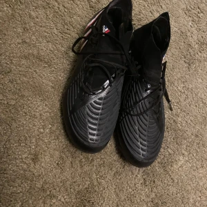 Svarta fotbollsskor från Adidas - Säljer ett par svarta Adidas fotbollsskor i bra skick. Skorna har en snygg design med snörning och mönstrad sula för bra grepp på planen. Perfekta för fotbollsträning eller match. Storlek och passform är normal. Storlek 42,5
