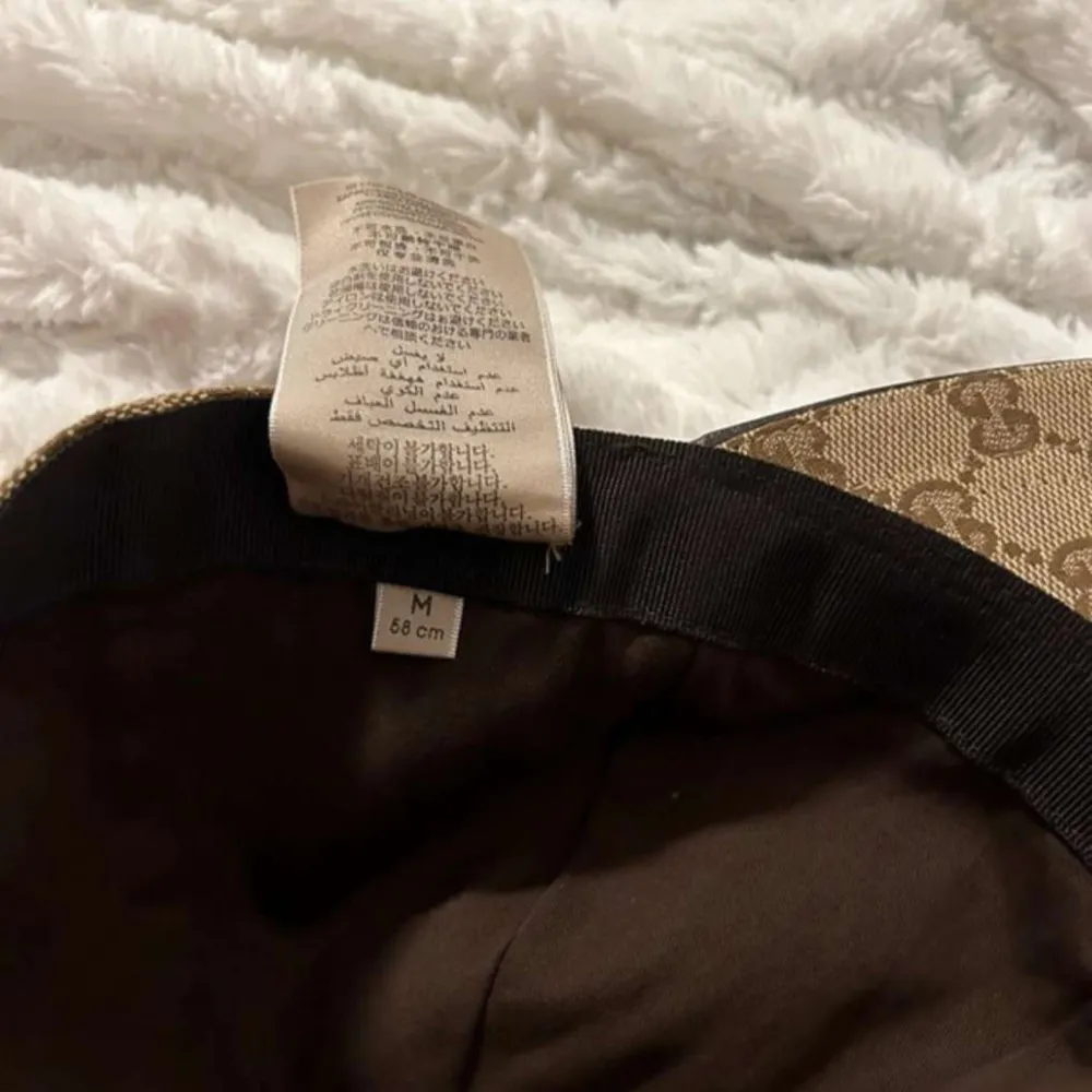 Säljer en snygg beige keps från Gucci med deras ikoniska monogrammönster. Kepsen har en justerbar rem baktill och klassiska gröna och röda ränder på sidan. Perfekt för att ge din outfit en lyxig touch!. Accessoarer.