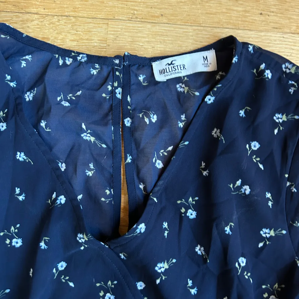 Säljer en superfin blå jumpsuit från Hollister med små blommor. Den har långa ärmar och en omlott-design framtill. Genomskinligt tyg i ryggen. Materialet är lätt och luftigt, vilket gör den bekväm att bära. 💙aldrig använd så toppen skick . Klänningar.