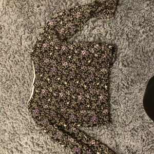 Blommig långärmad topp - Säljer en superfin blommig topp med lång ärm. Den har ett mönster i lila och vitt på en svart bakgrund. Perfekt för både vår och höst! Toppen är i bra skick och passar till både jeans och kjol. 🌸