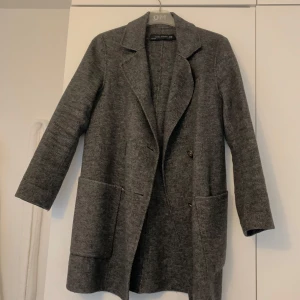 Grå kappa från Zara Woman - Säljer en stilren grå kappa från Zara Woman i storlek XS. Den har en klassisk design med långa ärmar och två stora fickor framtill. Perfekt för höst och vår. Kappan är i mycket bra skick  