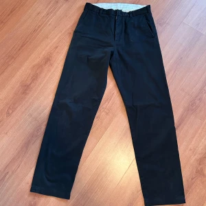 Svarta chinos från Arket  - Säljer ett par stilrena svarta chinos från Arket. Bild 3 visar hur de sitter på. De har en klassisk rak passform med dragkedja och knapp framtill. Perfekta för både formella tillfällen och kontoret. Ordinariepris ca 1200kr. Byxorna är i mycket bra skick och är i storlek Eu 46. Hör av er vid frågor eller funderingar! Pris går att diskutera!