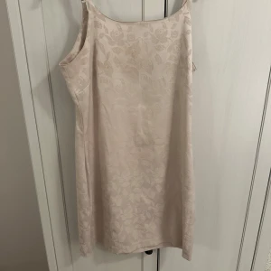 Beige klänning med blommigt mönster - Säljer en elegant beige klänning med ett subtilt blommigt mönster. Klänningen är ärmlös och har en smickrande passform som passar perfekt för sommarens fester. Materialet känns lyxigt och mjukt mot huden. Perfekt för en stilren och chic look!