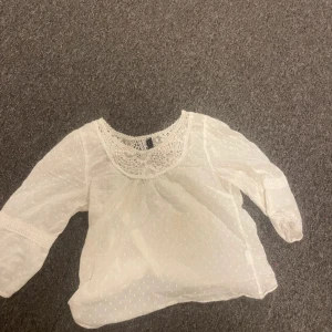 Vit blus med spetsdetaljer - Söt vit blus från vero Moda med spetsdetaljer runt halsen. Blusen har trekvartsärmar och ett diskret prickigt mönster. Den är i mycket bra skick och redo för en ny ägare!