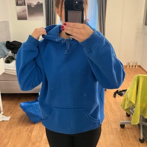 Blå hoodie i bra skick - Säljer en supermysig blå hoodie i bra skick. Den har en klassisk känguruficka och justerbar dragsko i huvan. Perfekt för chilliga dagar eller som ett extra lager under jackan. Passar både till vardags och för en avslappnad stil.