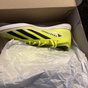 Gula Adidas fotbollsskor - Säljer ett par knallgula Adidas fotbollsskor i mycket bra skick. De har svarta detaljer och snörning, perfekt för inomhusfotboll. Skorna är lätta och designade för snabbhet på planen. Storlek är inte angiven, men de ser ut att vara i standard herrstorlek.