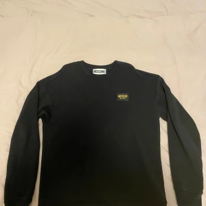 Moschino sweatshirt - Säljer en stilren svart tröja från Moschino i mycket bra skick. Den har långa ärmar och en liten Moschino-logga på bröstet. Perfekt för både vardag och fest! 🖤