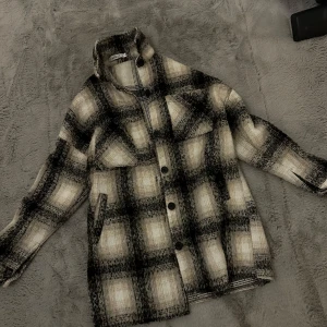 Rutig overshirt i ullmix - Säljer en supercool rutig overshirt i en skön ullmix. Den har en avslappnad passform med stora knappar och två bröstfickor. Perfekt för höst och vår när du vill ha något stilrent men ändå mysigt. Färgerna går i svart, grått och beige/vit, vilket gör den lätt att matcha med det mesta. 🖤🤍