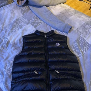 Svart dunväst från Moncler - Säljer en Moncler-väst. Västen är använd några gånger och köptes för 2400 kr via Plick. Dragkedjan kan ibland vara lite trög, men fungerar och går att stänga, vilket syns på bilden.  Vid snabb affär kan priset diskuteras.  Hör av dig vid intresse!