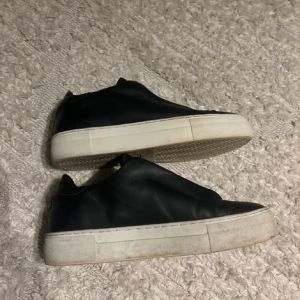 Svarta sneakers från Axel Arigato - Säljer ett par stilrena svarta sneakers från Axel Arigato. De har en vit sula och är i bra skick. Perfekta för både vardag och fest! Skorna är gjorda i skinn och har en minimalistisk design utan snörning.