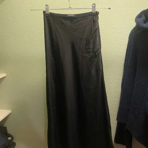 Svart långkjol från Amisu - Säljer en elegant svart långkjol från Amisu i storlek EU 34. Kjolen har en klassisk och tidlös design, perfekt för både vardag och fest. Materialet känns mjukt och följsamt, vilket ger en bekväm passform. Passar utmärkt till höst- och vintergarderoben.