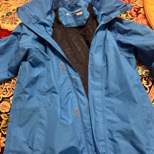 Blå vindjacka från Everest - Säljer en blå vindjacka från Everest i storlek S. Jackan har en praktisk dragkedja och är perfekt för blåsiga dagar. Den är i bra skick och har ett meshfoder för extra komfort. Perfekt för vår och höst!